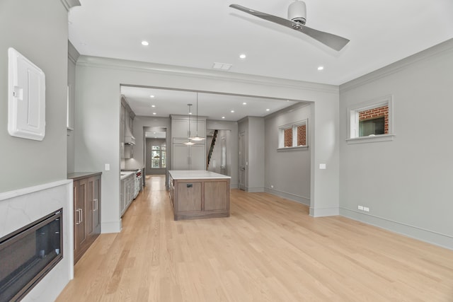 kitchen featuring a high end fireplace, a center island, ornamental molding, ceiling fan, and light wood-type flooring