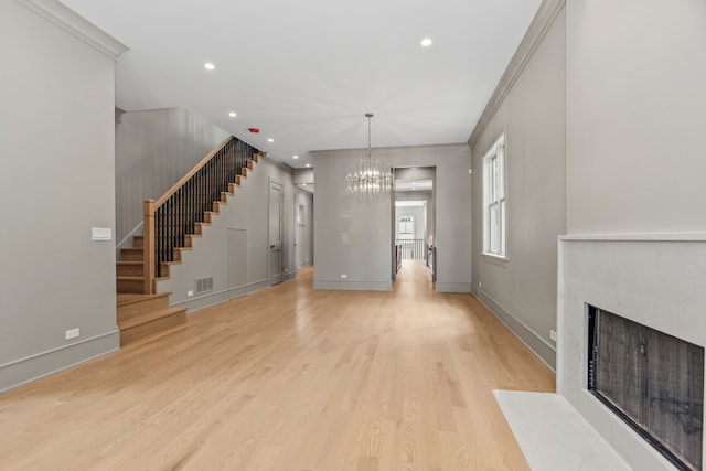 unfurnished living room featuring crown molding, a premium fireplace, light hardwood / wood-style flooring, and an inviting chandelier