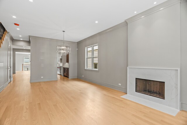 unfurnished living room with a fireplace, crown molding, a chandelier, and light hardwood / wood-style floors