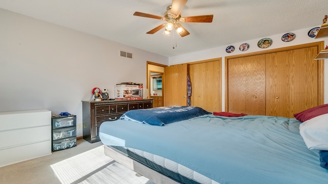 carpeted bedroom featuring a textured ceiling, two closets, and ceiling fan