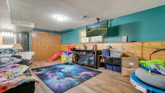 interior space with a textured ceiling, wood walls, and light wood-type flooring