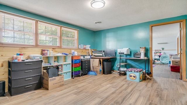 office with a textured ceiling, light hardwood / wood-style flooring, and wood walls