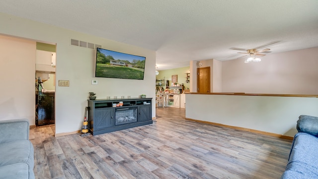 living room featuring a textured ceiling, ceiling fan, and light wood-type flooring