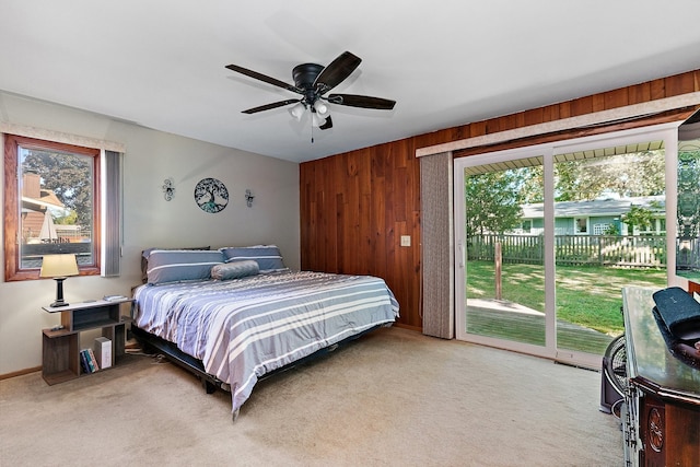 carpeted bedroom featuring access to outside, wood walls, and ceiling fan