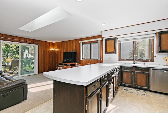 kitchen featuring stainless steel dishwasher, sink, wooden walls, and a skylight