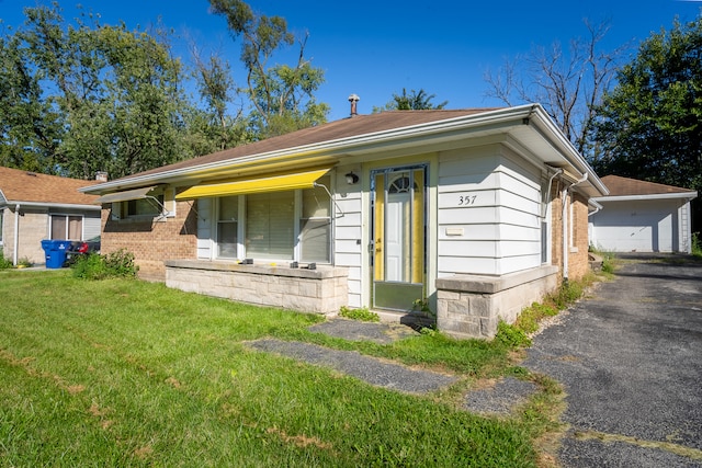 ranch-style house featuring covered porch, an outbuilding, a garage, and a front lawn