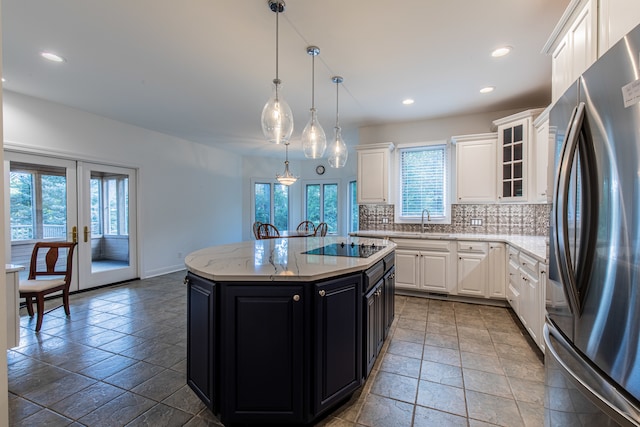 kitchen featuring stainless steel refrigerator, light stone counters, a center island, french doors, and white cabinets