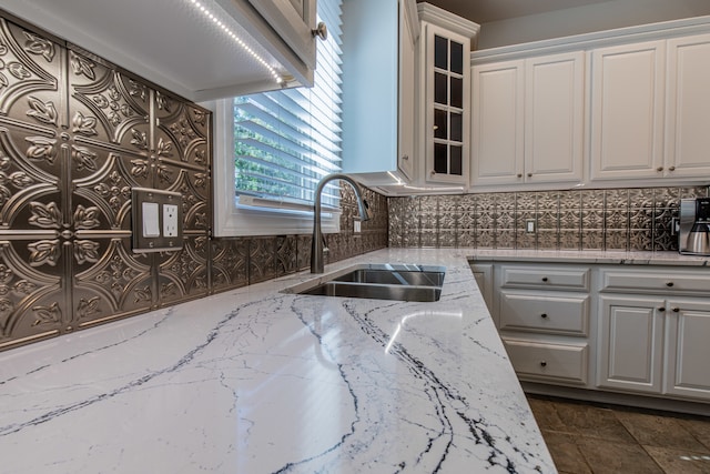 kitchen with tasteful backsplash, light stone counters, sink, and white cabinets