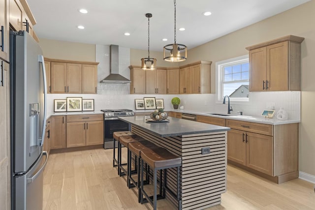 kitchen featuring stainless steel appliances, light wood-style flooring, a sink, and wall chimney range hood