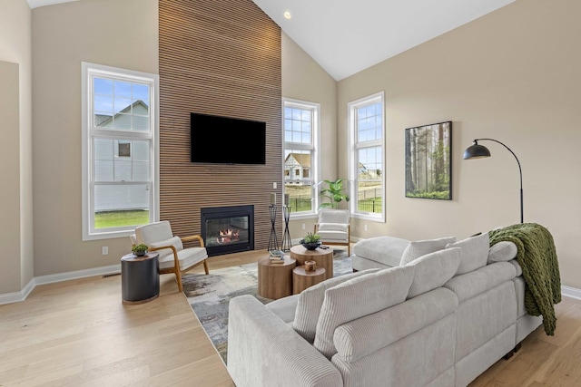 living area featuring light wood-style floors, baseboards, a large fireplace, and high vaulted ceiling
