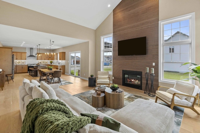 living area featuring baseboards, recessed lighting, light wood-style floors, a large fireplace, and high vaulted ceiling