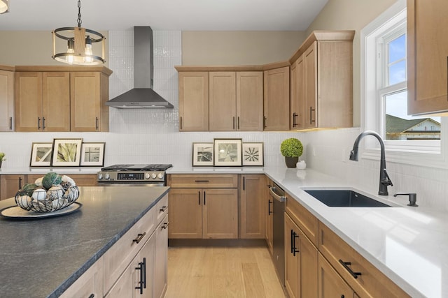 kitchen featuring wall chimney range hood, a sink, light wood-style floors, decorative backsplash, and appliances with stainless steel finishes