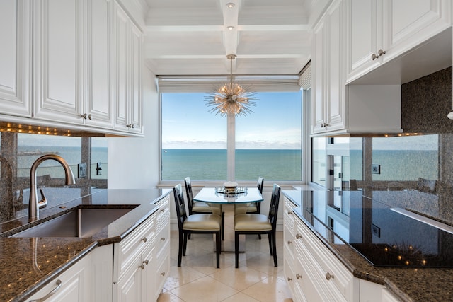 kitchen featuring white cabinetry, sink, a water view, and decorative light fixtures