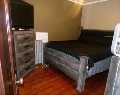 bedroom with dark hardwood / wood-style floors and radiator heating unit