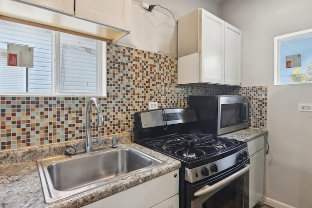 kitchen with appliances with stainless steel finishes, white cabinetry, sink, and decorative backsplash