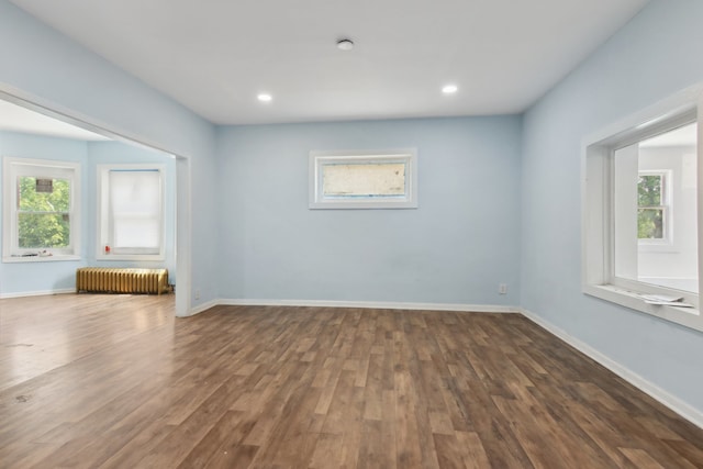 unfurnished living room featuring a wealth of natural light, radiator, and dark hardwood / wood-style flooring