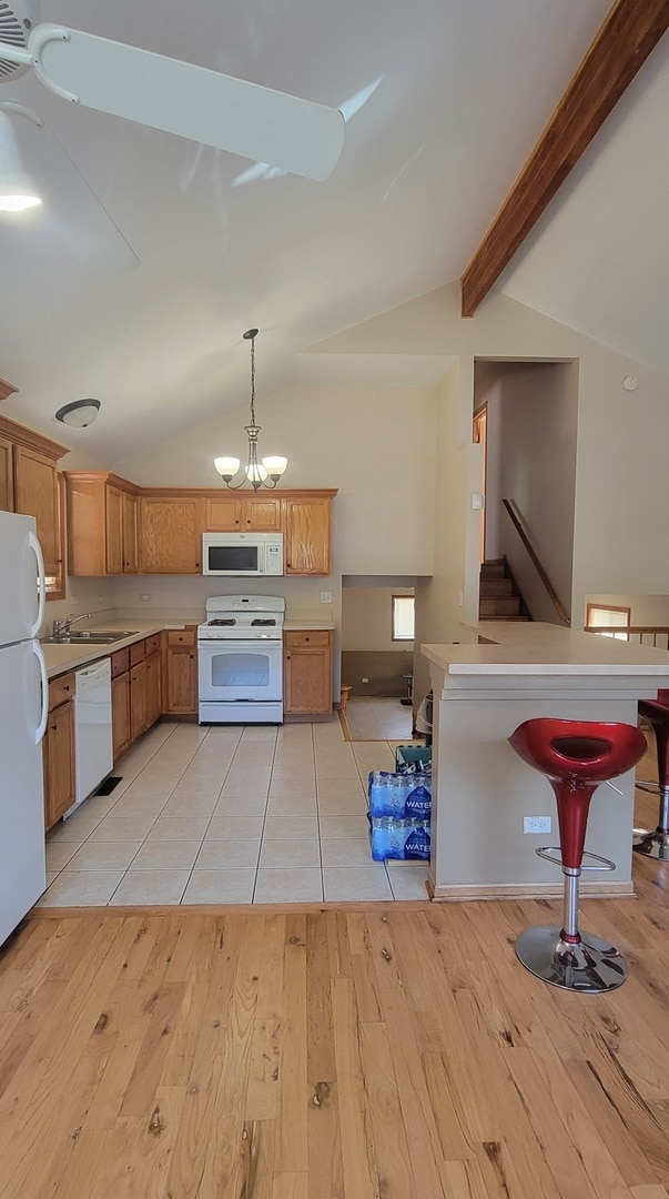 kitchen featuring decorative light fixtures, white appliances, a kitchen breakfast bar, and light hardwood / wood-style flooring