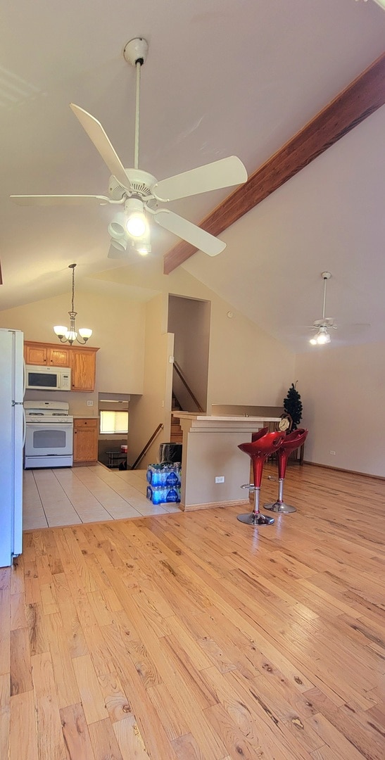 interior space with ceiling fan with notable chandelier, lofted ceiling with beams, and light hardwood / wood-style floors