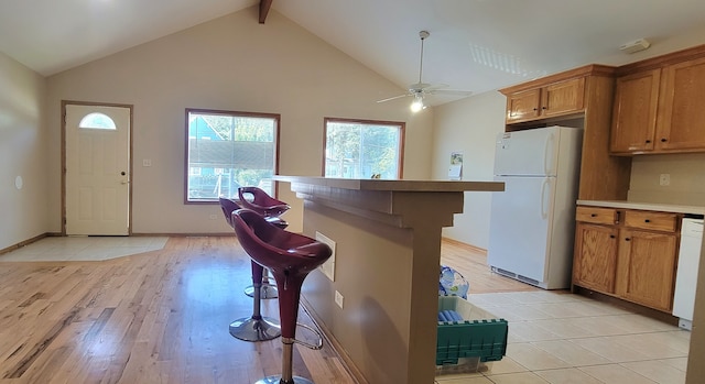 kitchen with light wood-type flooring, white refrigerator, ceiling fan, and a kitchen bar