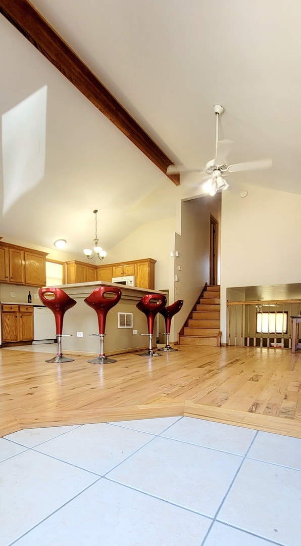 interior space with light wood-type flooring, ceiling fan with notable chandelier, high vaulted ceiling, and beam ceiling