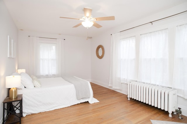 bedroom featuring multiple windows, radiator, ceiling fan, and light wood-type flooring