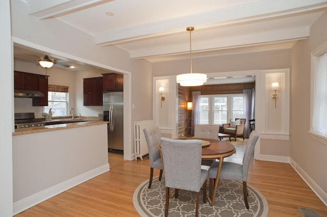 dining space with beam ceiling, radiator, sink, and light wood-type flooring