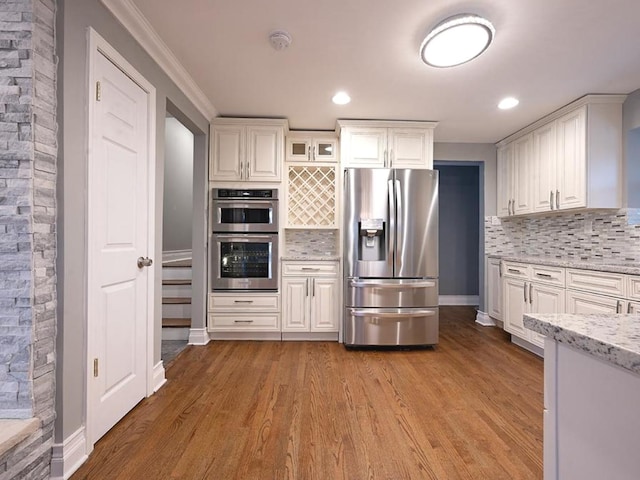 kitchen with light stone countertops, appliances with stainless steel finishes, backsplash, light hardwood / wood-style floors, and white cabinets