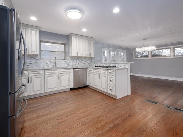 kitchen featuring kitchen peninsula, appliances with stainless steel finishes, white cabinetry, light hardwood / wood-style flooring, and pendant lighting