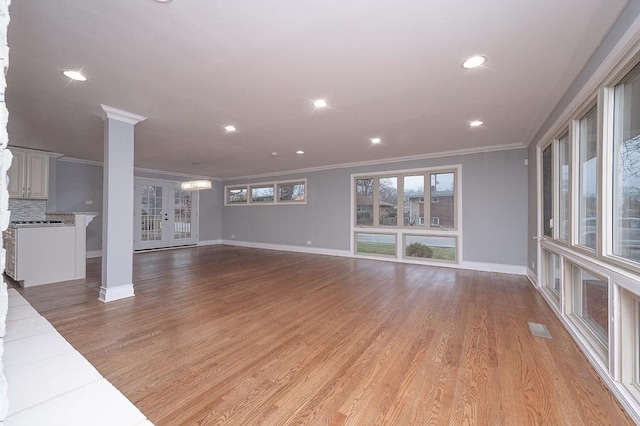 unfurnished living room featuring an inviting chandelier, ornamental molding, ornate columns, and light hardwood / wood-style floors