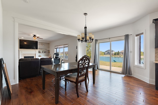 dining area with built in features, dark wood-type flooring, ceiling fan with notable chandelier, and a water view