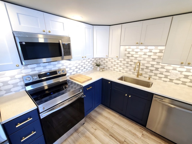 kitchen featuring blue cabinetry, white cabinetry, sink, decorative backsplash, and appliances with stainless steel finishes