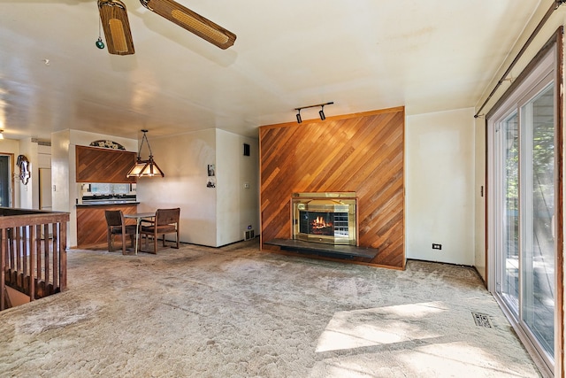 living room featuring carpet flooring, wooden walls, ceiling fan, and track lighting