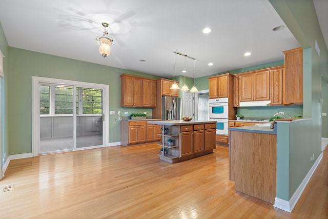 kitchen with light hardwood / wood-style floors, stainless steel refrigerator with ice dispenser, a kitchen island, decorative light fixtures, and double oven