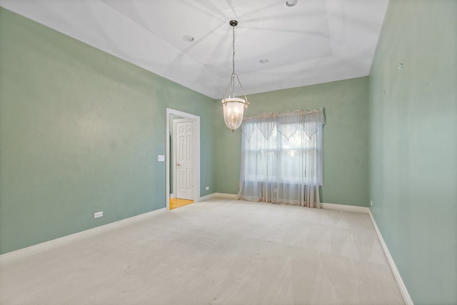 carpeted empty room with an inviting chandelier and a tray ceiling