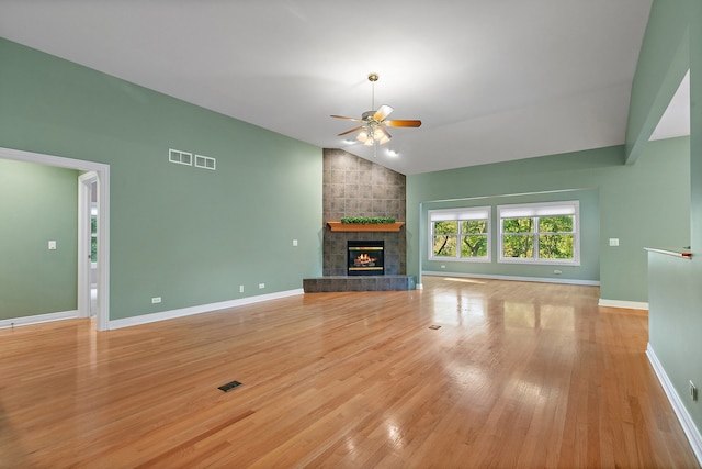 unfurnished living room featuring light wood-type flooring, vaulted ceiling, a tiled fireplace, and ceiling fan