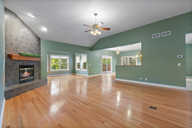 unfurnished living room with tile walls, a tile fireplace, ceiling fan with notable chandelier, vaulted ceiling, and light hardwood / wood-style flooring