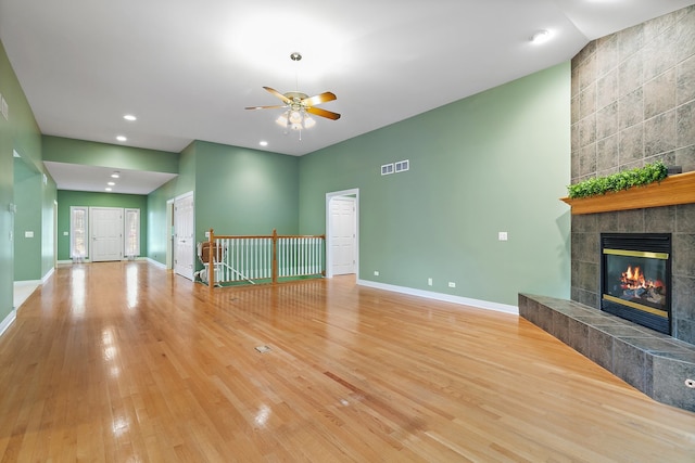 unfurnished living room featuring ceiling fan, vaulted ceiling, light hardwood / wood-style floors, and a tile fireplace