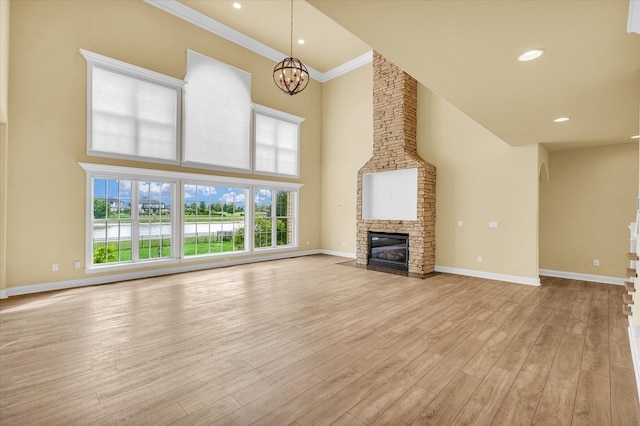 unfurnished living room featuring a fireplace, an inviting chandelier, light wood-type flooring, a high ceiling, and ornamental molding