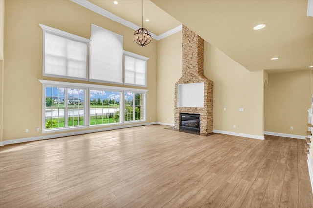 unfurnished living room with a high ceiling, a notable chandelier, a stone fireplace, light wood-style flooring, and baseboards