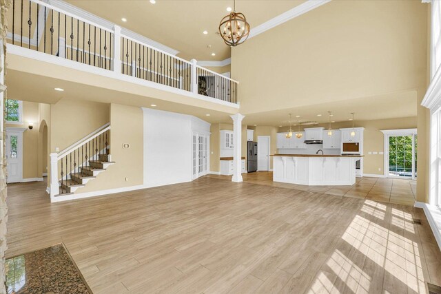 unfurnished living room featuring light wood-style floors, baseboards, ornamental molding, a towering ceiling, and stairs