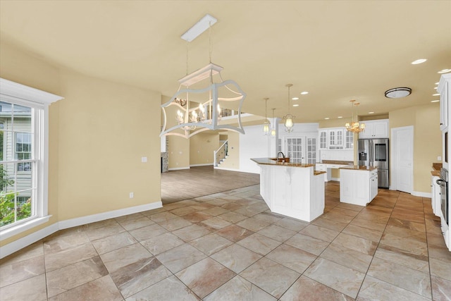 kitchen featuring a wealth of natural light, a kitchen island with sink, a notable chandelier, and stainless steel fridge with ice dispenser