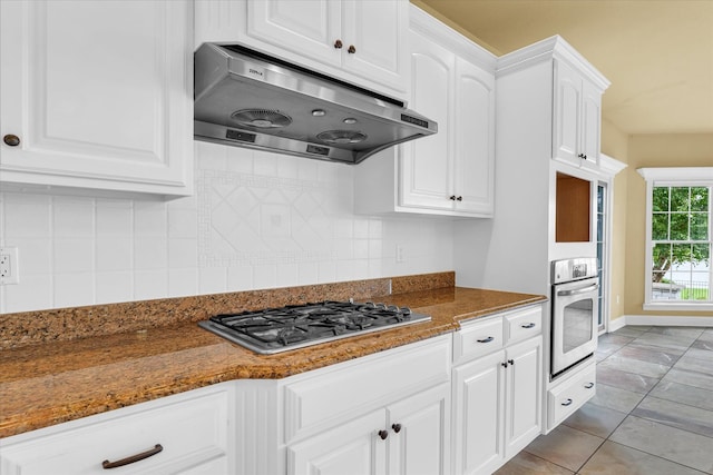 kitchen featuring dark stone countertops, light tile patterned floors, stainless steel appliances, decorative backsplash, and white cabinets