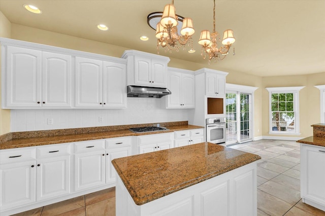 kitchen with white cabinets, under cabinet range hood, an inviting chandelier, gas cooktop, and stainless steel oven