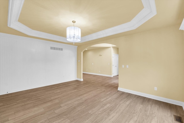 spare room with ornamental molding, light hardwood / wood-style flooring, a tray ceiling, and an inviting chandelier