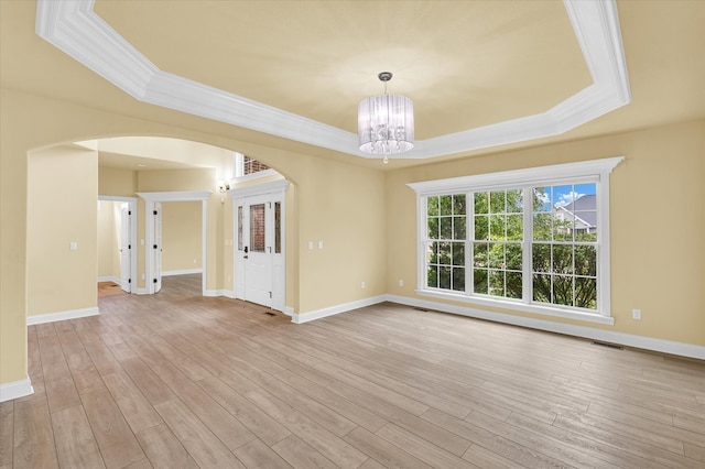 empty room featuring a raised ceiling, an inviting chandelier, and light wood-type flooring