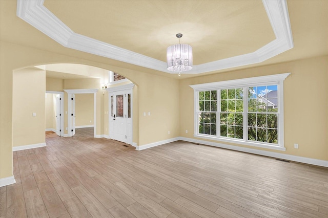 unfurnished room featuring a raised ceiling, an inviting chandelier, ornamental molding, and arched walkways