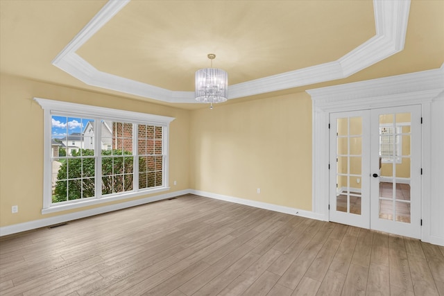 spare room featuring french doors, light hardwood / wood-style flooring, a raised ceiling, and a chandelier