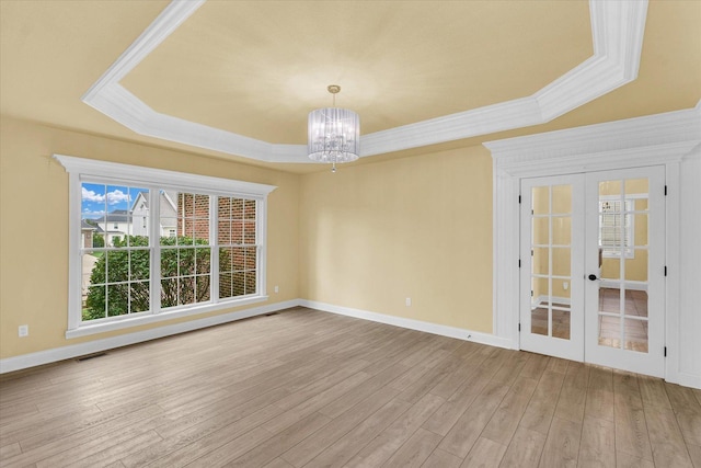 spare room featuring wood finished floors, a raised ceiling, a chandelier, ornamental molding, and french doors