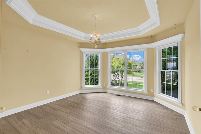 empty room featuring light wood-type flooring, a raised ceiling, ornamental molding, and a chandelier