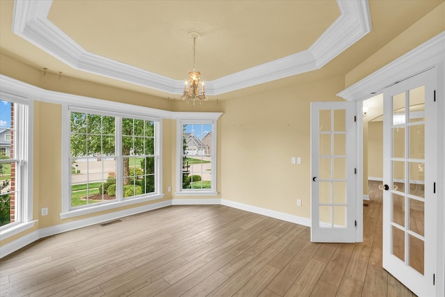 spare room with a raised ceiling, an inviting chandelier, french doors, crown molding, and light wood-type flooring